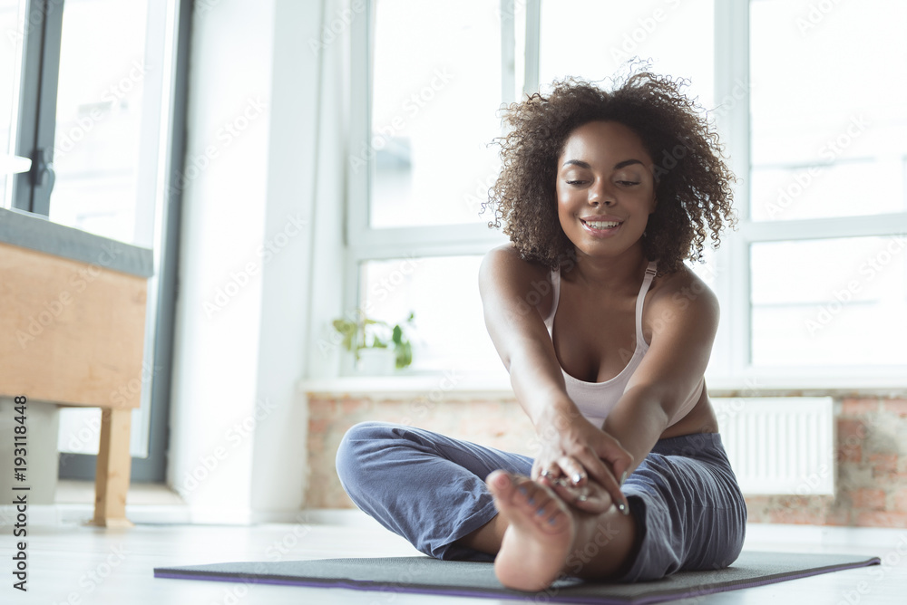 Portrait of full length outgoing young african girl engaging in sports activities on floor in cozy room. Copy space Portrait of full length outgoing young african girl engaging in sports activities on floor in cozy room. Copy space
