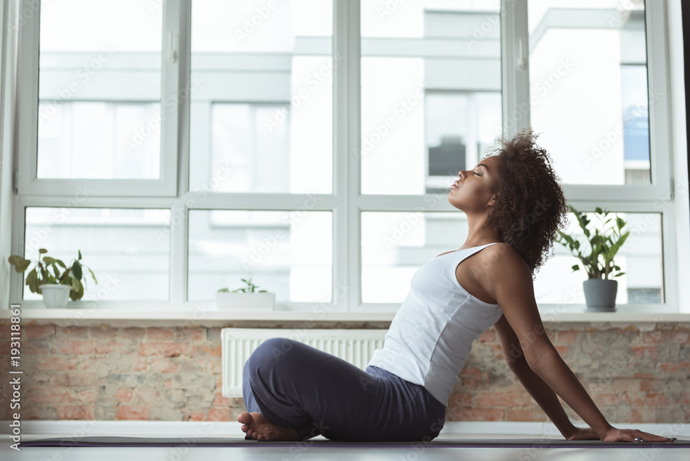 Side view serene girl doing exercise on mat in cozy room. She sitting on floor Side view serene girl doing exercise on mat in cozy room. She sitting on floor