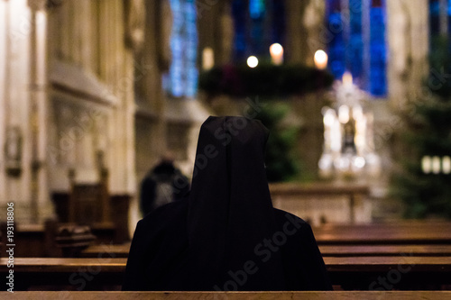 old sister nun praying at dark church or cathedral during christmas photo