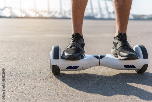 Close up male feet wearing modern sneakers going on hoverboard at street. Copy space