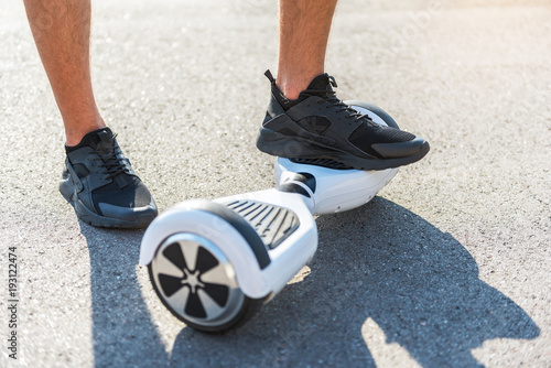 Close up boy leg standing on hoverboard while another situating on asphalt. Digital device concept