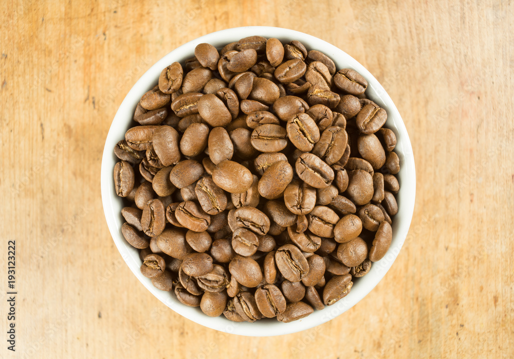 Fototapeta premium Light roast brown coffee beans in a white bowl on a wooden table top