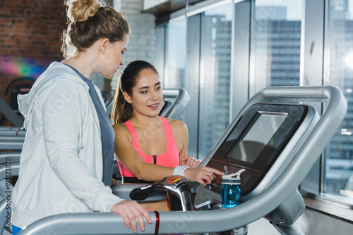 trainer adjusting treadmill before training of overweight woman