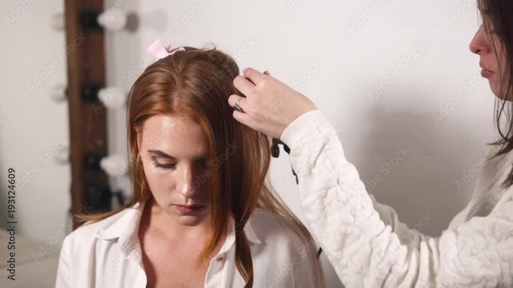 Stylist is curling hair of client woman using curling iron. She is warming one strand of hair and touching curl, client is sitting calmly Stylist is curling hair of client woman using curling iron. She is warming one strand of hair and touching curl, client is sitting calmly