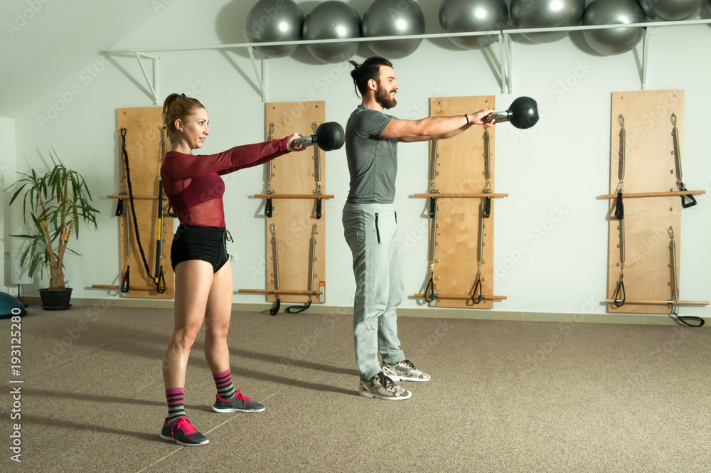 Fototapeta premium Young couple kettle bell fitness exercise in the gym, selective focus