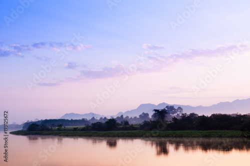 Beautiful tranquil river scene in evening or morning with warm sunset or sunrise light, mountain view reflected on calm river surface © PixHound