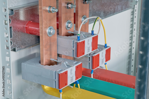 Copper busbars with current transformers on them in an electric Cabinet. Copper busbars are bolted to the mounting panel. Marking on wires and bus bars of red, green and yellow.