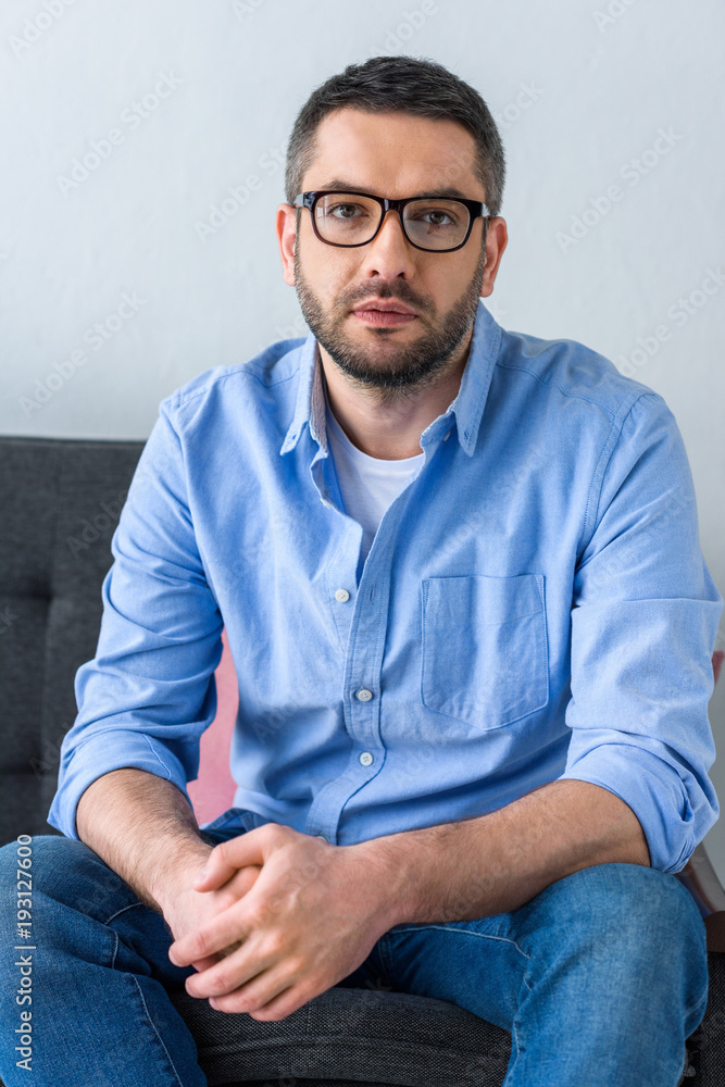 Obraz premium portrait of man in eyeglasses sitting on sofa and looking at camera