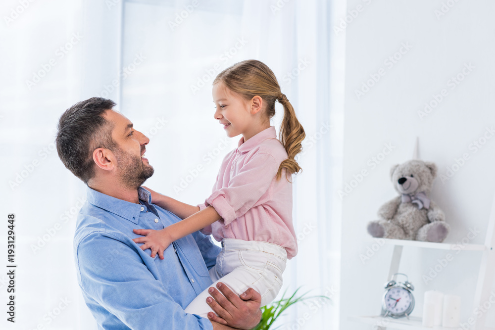 Fototapeta premium side view of happy father holding little daughter in hands at home