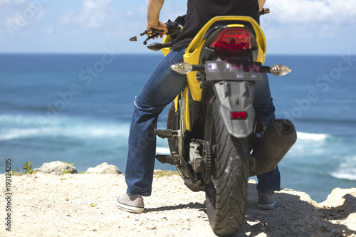 Young handsome man sitting on motorcycle on the tropical beach.