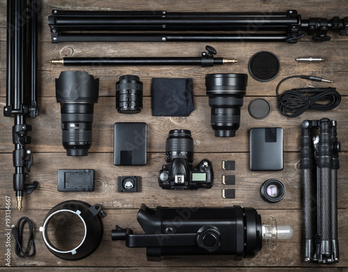 Set of the camera and photography equipment (lens, tripod, filter, flash, memory card, hard desk, reflector) on wood desk. Professional photographer accessories background.
