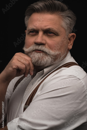 thoughtful senior man in white shirt with suspenders isolated on black