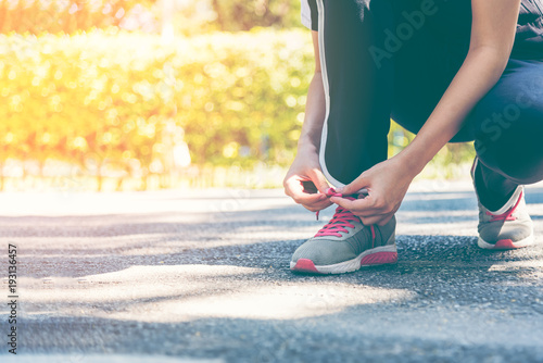 Female runner preparing to go for a jog outdoors. Young women tying shoelace prepare for jogging as an exercise in a sunny day.