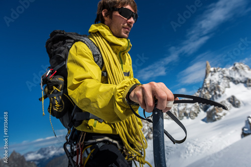 Young man keep ice ax in right hand. Hand and ice ax is sharp, other is blured photo