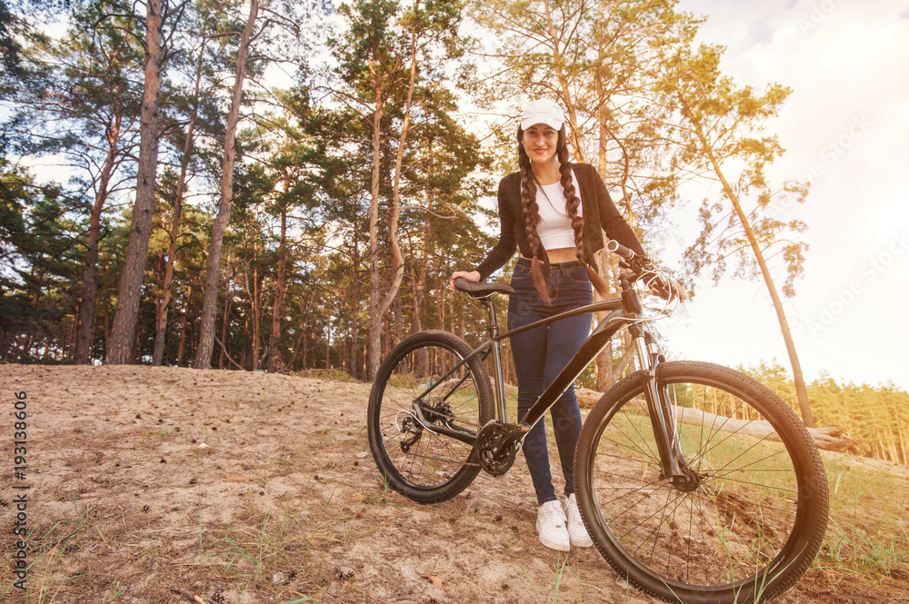 Bicyclist female on the bike in spring riding in the forest. Beautiful girl and her bicycle in the landscape. She hugs her bike and poses to the operator. Sunset time