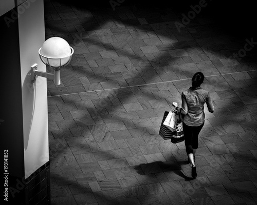 SHOPPING WOMAN IN MALL UNDER SKYLIGHT SHADOWS B&W