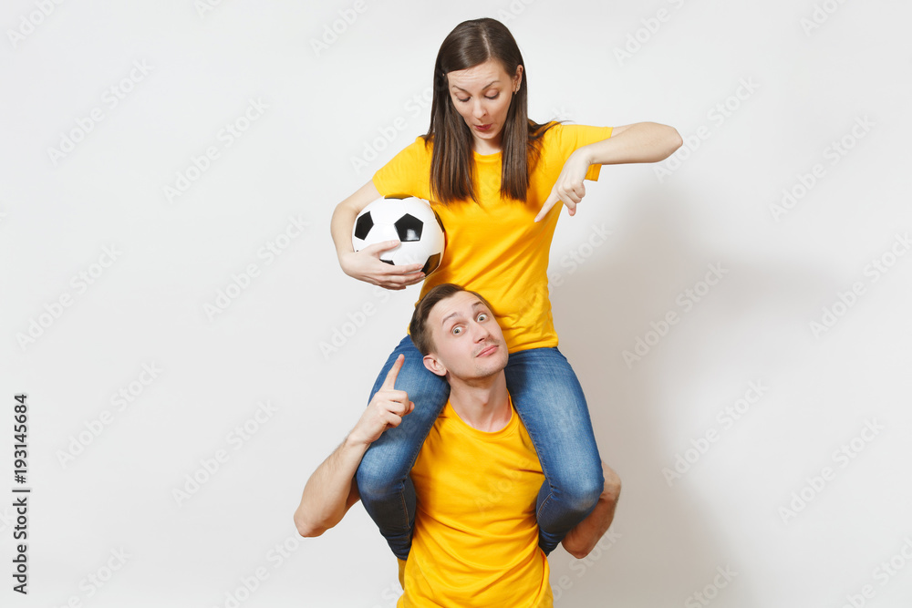 Inspired young couple, woman sit on man shoulders, fans with soccer ball cheering favorite football team expressive gesticulating hands isolated on white background. Family leisure, lifestyle concept.