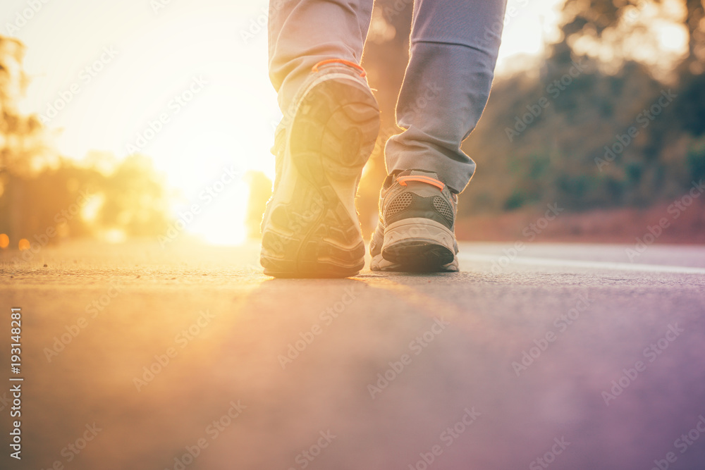 man walking on road with sun light flare ,close up on shoe jogging workout wellness after work - obrazy, fototapety, plakaty 
