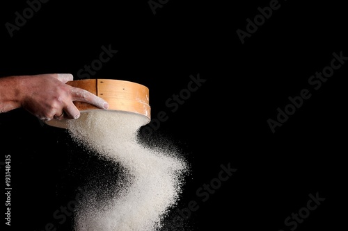 men's hands are sifting flour through a sieve on black background photo