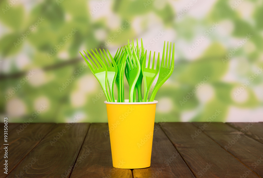 Disposable yellow forks stand in glass, on wooden table Disposable yellow forks stand in glass, on wooden table