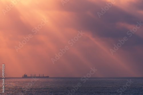 sunrays on the ocean with freighter ship