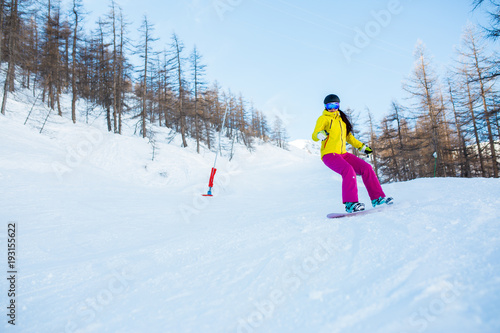 Picture of athlete woman wearing helmet and mask snowboarding from snowy slope with trees