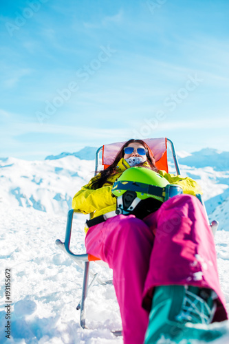 Pictures of sporty woman with helmet resting on chair in winter resort