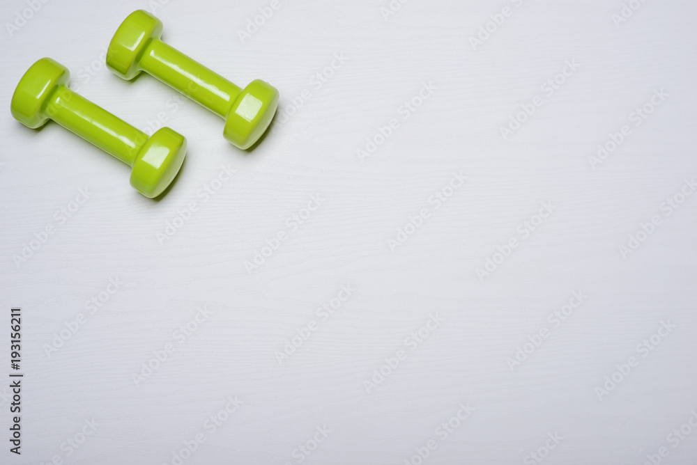 Two dumbbells of green color lie on a white background with a tree texture Two dumbbells of green color lie on a white background with a tree texture