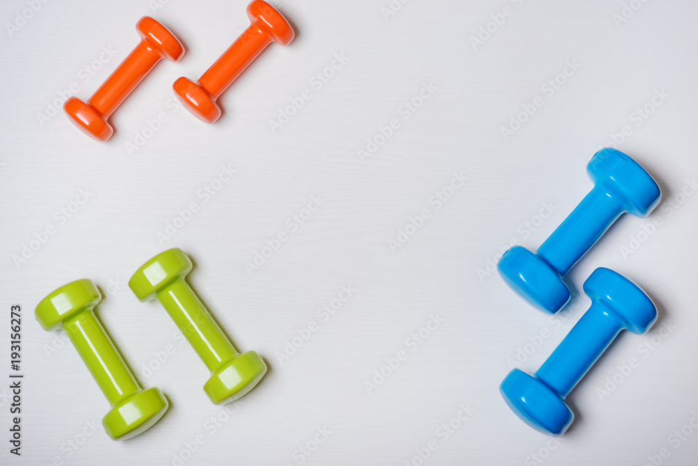 many blue green and one orange in the middle dumbbells on a white background ,concept preparing to fitness sports equipment top view mock up