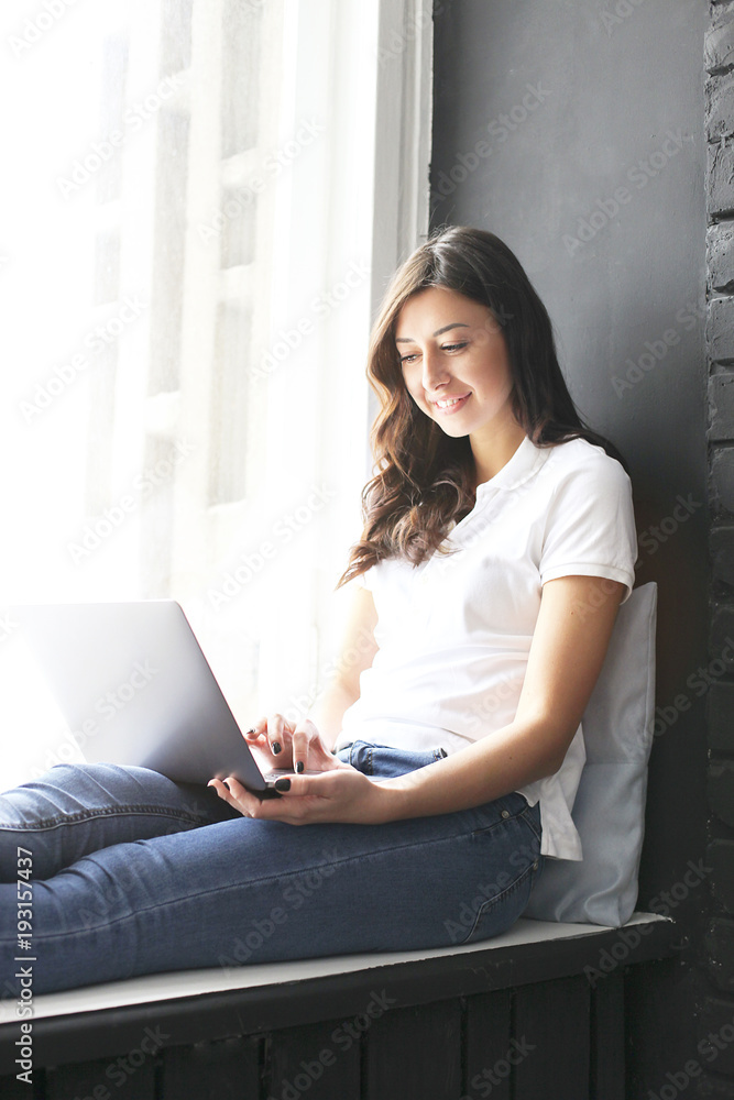 Happy millennial girl w/ laptop on windowsill. Portrait of young woman with diastema gap between teeth. Beautiful smile. Minimal interior, black brick textured wall background, loft style. Copy space. Happy millennial girl w/ laptop on windowsill. Portrait of young woman with diastema gap between teeth. Beautiful smile. Minimal interior, black brick textured wall background, loft style. Copy space.