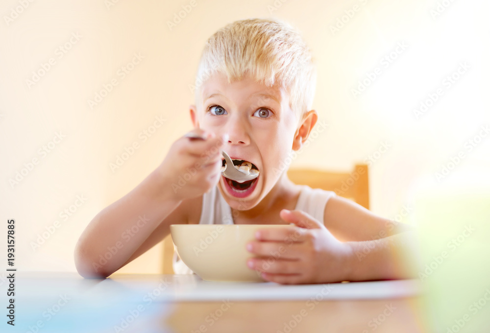Kid Eating Food Cereals on Table with Spoon, Looking at camera Kid Eating Food Cereals on Table with Spoon, Looking at camera