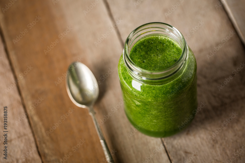 Green spinach juice jar on a rustic wooden table and spoon Green spinach juice jar on a rustic wooden table and spoon