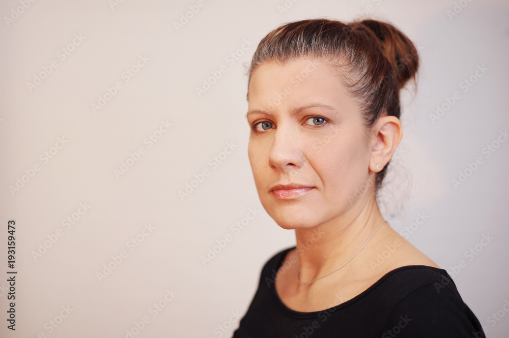 Portrait of a sad middle-aged woman on a gray background. She is sad because her hair is already partly gray Portrait of a sad middle-aged woman on a gray background. She is sad because her hair is already partly gray