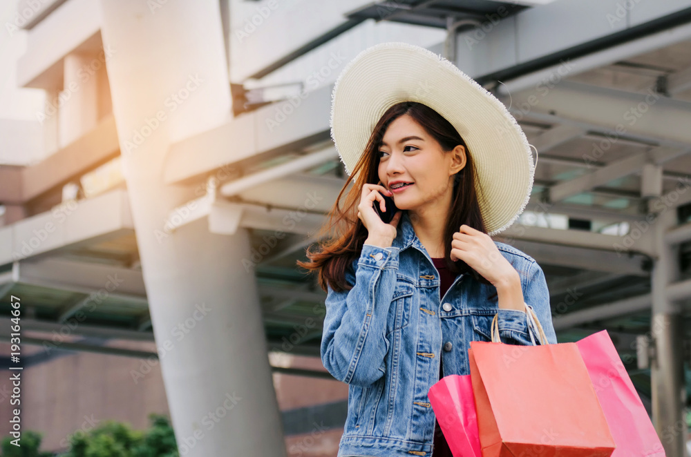 Fototapeta premium cheerful asian young woman making phone call on mobile smart phone with shopping bags in big city, black friday, technology, internet, winter sale, promotion, payment and shopping online concept