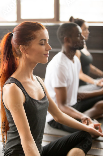 Group of young sporty afro american and caucasian people practicing yoga lesson, sitting in Easy Seat exercise, Sukhasana pose, working out, students training in sport club, studio close up