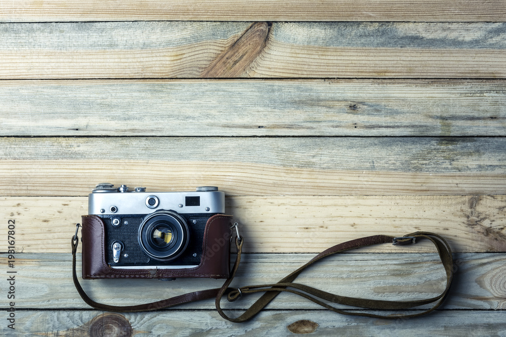 Old vintage film photo camera with brown leather strap on grunge wooden table. Photographe concept background