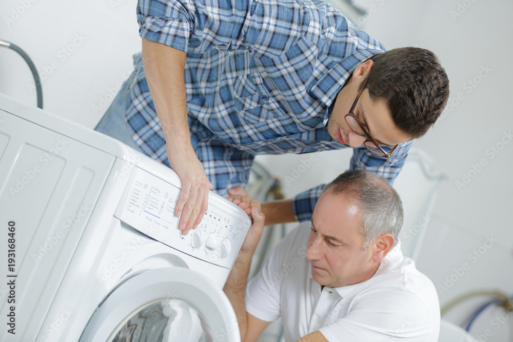 handyman and colleague fixing a washing machine in the kitchen handyman and colleague fixing a washing machine in the kitchen