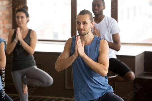 Group of young afro american and caucasian sporty people practicing yoga with instructor standing in Vrksasana exercise, Tree pose, working out, indoor close up, studio. Healthy lifestyle concept © fizkes