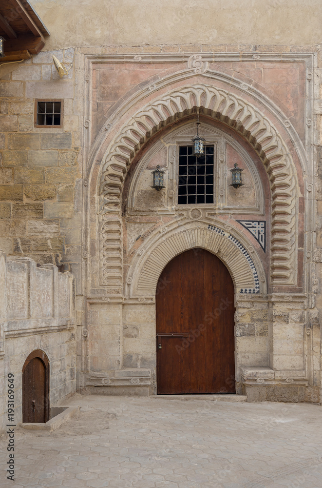 Naklejka premium Gate of Darb Al Labana alley, a Bahari Mameluke era gate with small window covered with iron bars and decorated with wooden and stone decorative elements with geometric designs