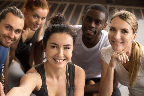 Young smiling sporty multiracial friends taking group selfie photo holding looking at camera, happy healthy diverse fit people making self-portrait after working out together in gym, view from camera