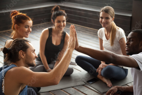 Fit sporty smiling african and caucasian men giving high five at group training, motivated diverse multiracial friends join hands together as concept of team support in fitness yoga studio teamwork
