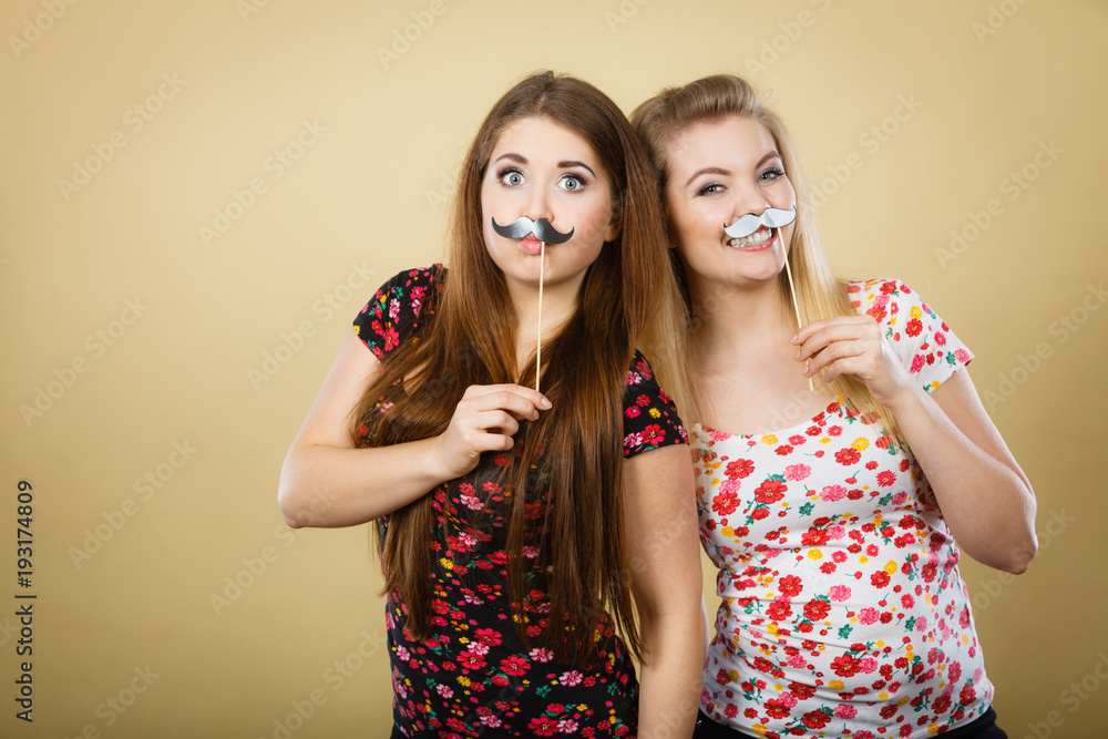 Two happy women holding fake moustache on stick Two happy women holding fake moustache on stick