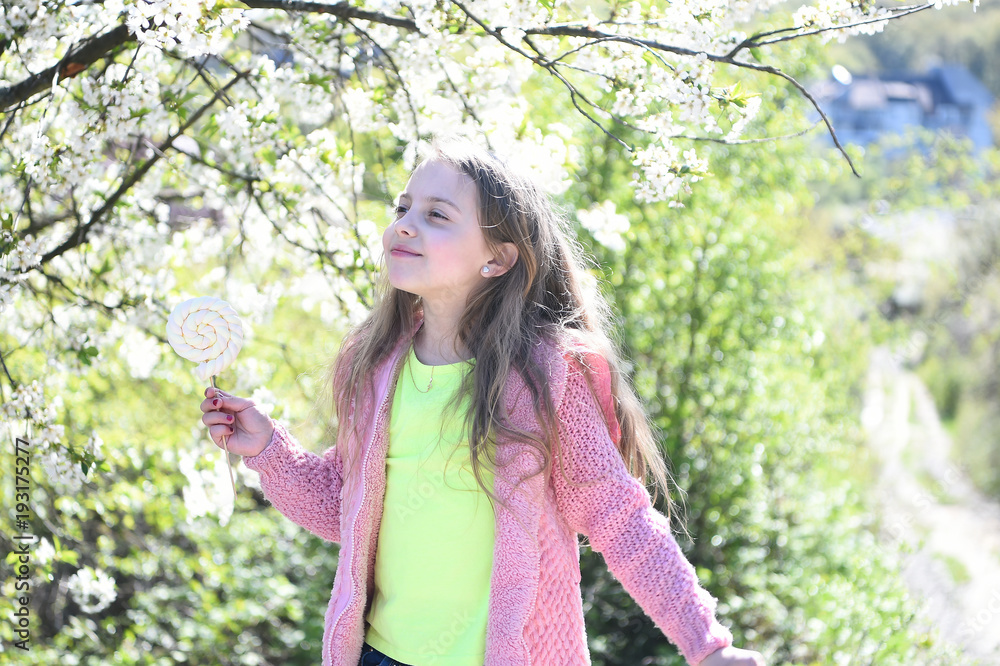 Girl with lollipop candy walking in park on blossoming background Girl with lollipop candy walking in park on blossoming background