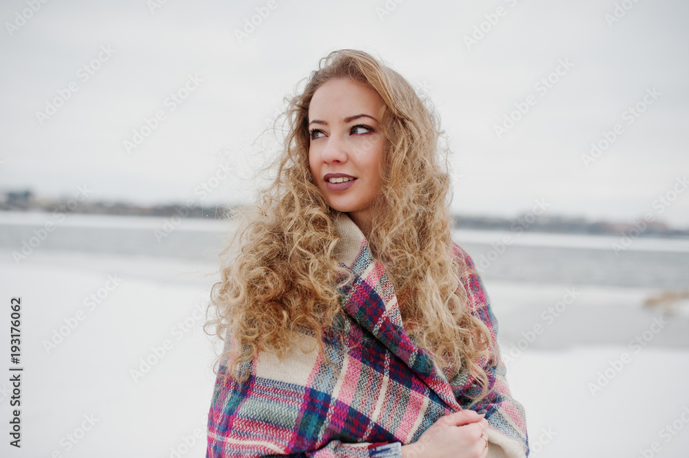 Curly blonde girl in checkered plaid against frozen lake at winter day. Curly blonde girl in checkered plaid against frozen lake at winter day.