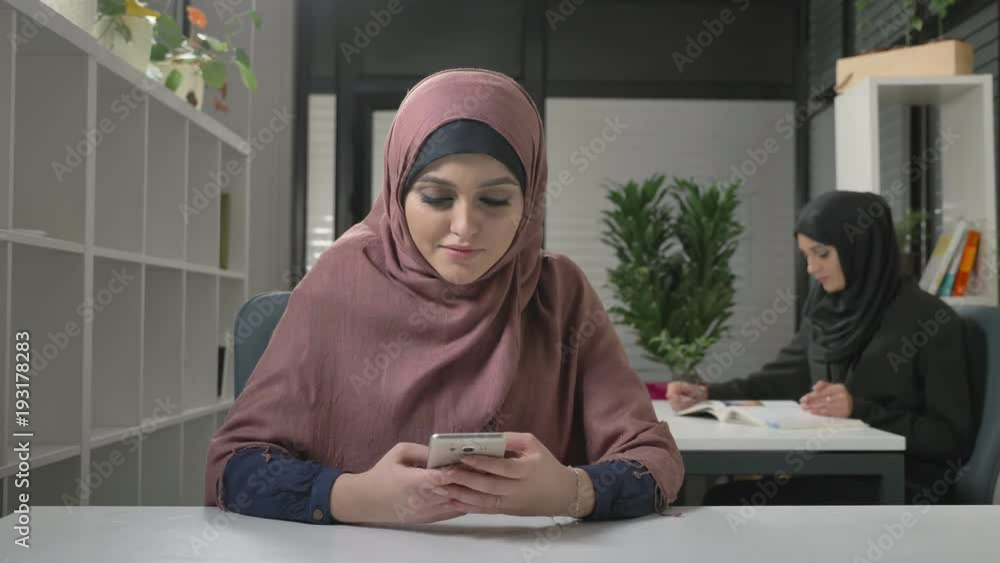 Beautiful young girl in red hijab sits in office and uses smartphone. Arab women in the office. 60 fps Beautiful young girl in red hijab sits in office and uses smartphone. Arab women in the office. 60 fps