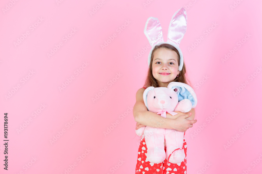 Happy girl holding rabbit toy on pink background