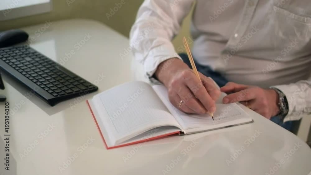 Business man working at a computer, making notes in a notebook with a pen close-up Business man working at a computer, making notes in a notebook with a pen close-up