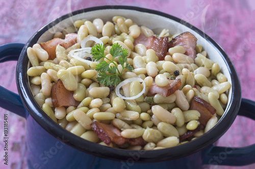 Blue vintage pot of Baked flageolet Beans With Smoked Pork Ribs on an old pink wooden board photo