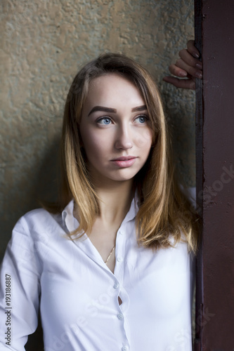 Attractive brunette model in white shirt posing in the entrance of the apartment building