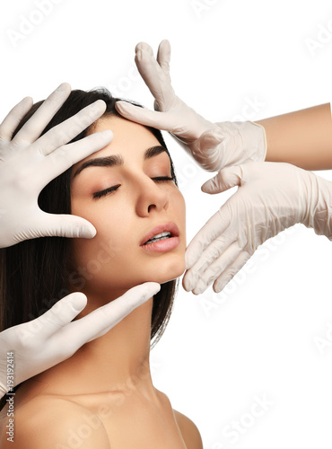 Doctor hands in medical gloves touch beautiful young woman face with closed eyes after plastic surgery 